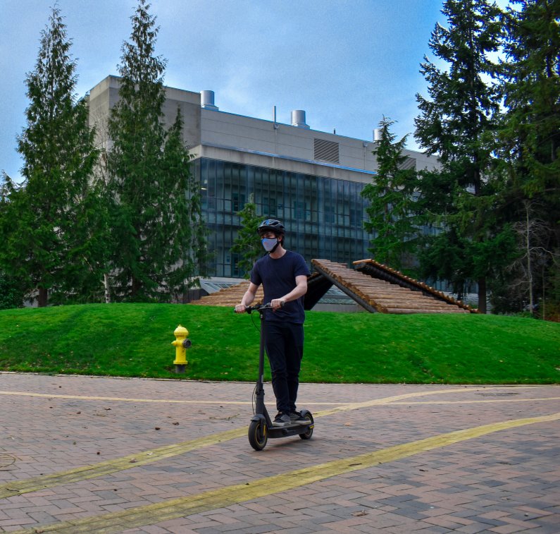 A masked student rides an electric scooter past the Log Ramps sculpture on Western's campus.