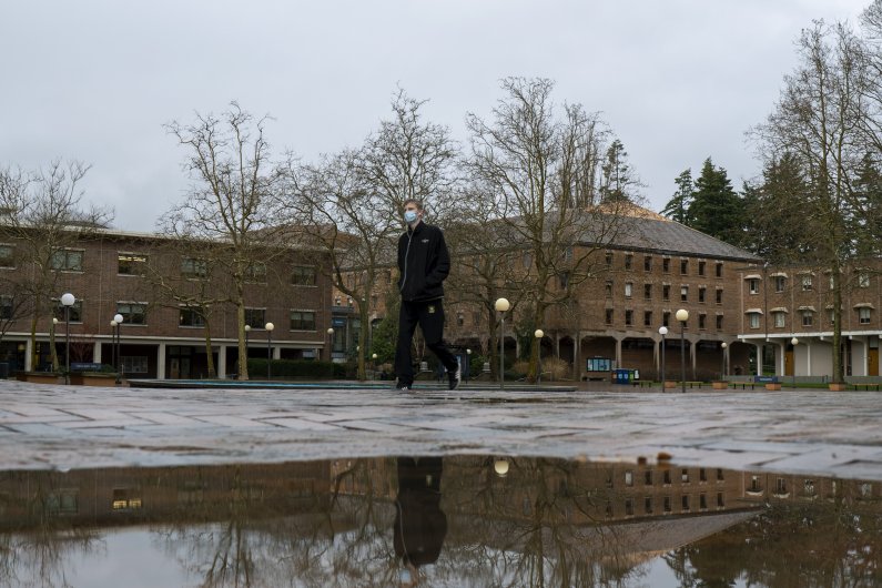 A masked student is reflected in a puddle as he walks across Red Square.