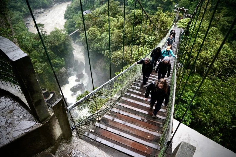 Students walk on a suspension bridge toward the Pailon del Diablo waterfall.