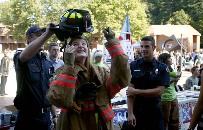 Western Washington University freshman Katie Coty tries on some fire gear at the annual info fair on campus Sept. 20. Helping Coty are Western students and volunteer firefighters Joe Kowall, left, and Seth Holsinger. Photo by Matthew Anderson | WWU