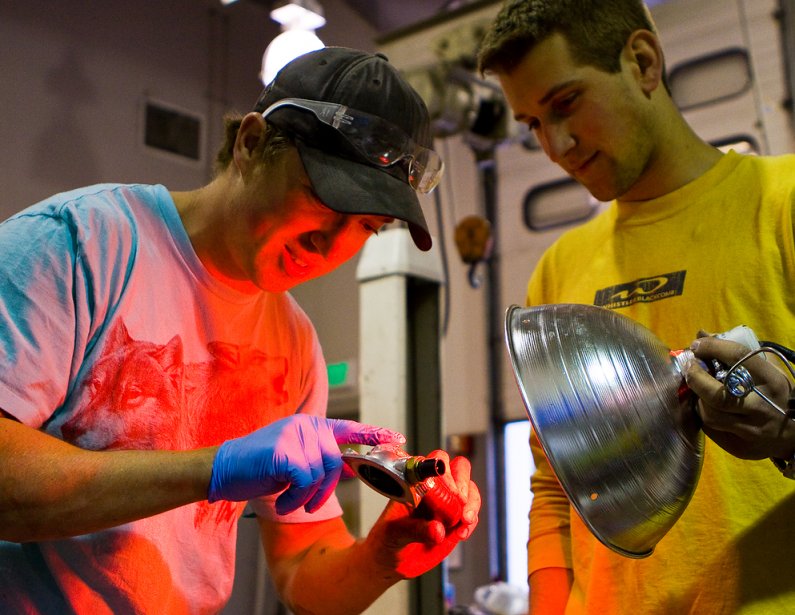 Kyle Foley, left, smears five-minute epoxy onto a flange housing the thermostat to the engine of Viking 45 while Brent Wise holds a heat lamp intended to help the hardening process on April 20. Photo by Jon Bergman | University Communications intern