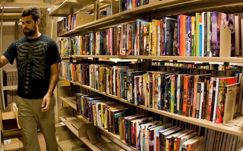 WWU student Devin Spencer organizes books on shelves in Wilson Library. The sale of these children's books will benefit the English Department. Photo by Jon Bergman | WWU intern