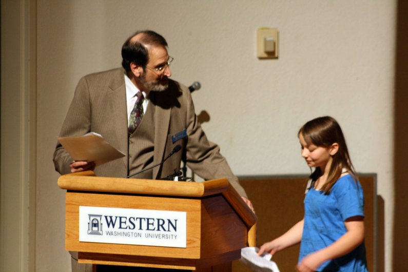 Ray Wolpow, left, a faculty member of Woodring College of Education at WWU, welcomes Emma Bruntil of Acme Elementary School to the stage to read a poem she wrote about Noemi Ban. Photo by Shea Taisey | University Communications intern