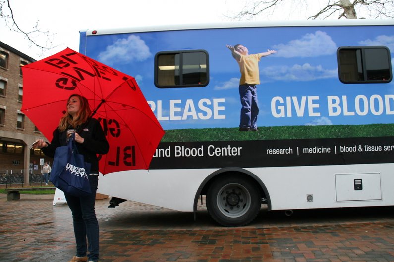 Western Washington University freshman Rosalee Daughtry, 19, holds an umbrella bearing the words "GIVE BLOOD" outside the mobile donation station in Red Square on Tuesday, April 19. Photo by David Gonzales | University Communications intern