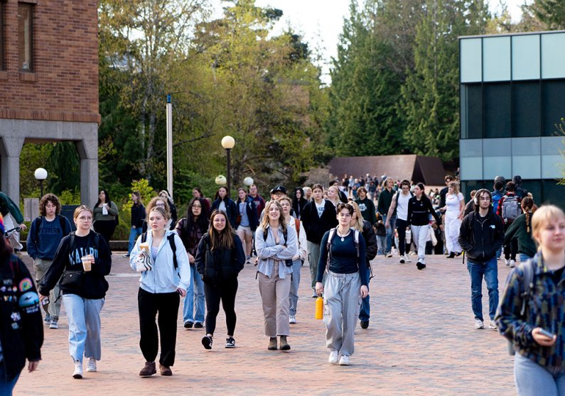 Students walk to class down the red brick walkway south of Red Square, looking south; in the background is the corner of Carver Gym.