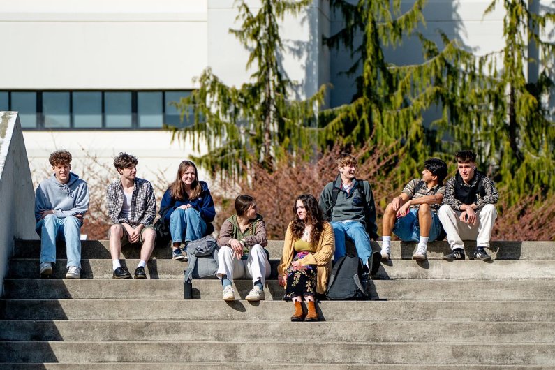 A group of students sits, chatting and happy, on the steps near the Communications Lawn.