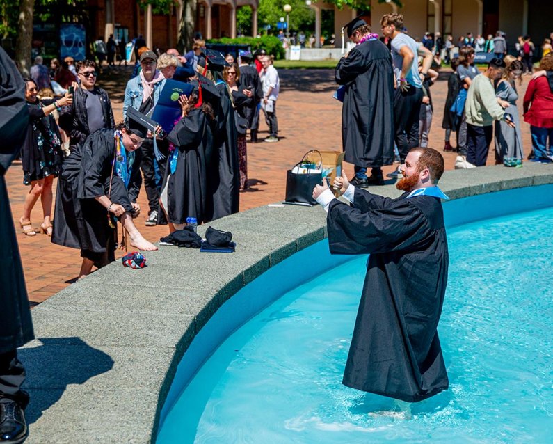 A new alumnus wades in Fisher Fountain in his robe