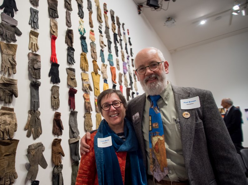 Carol Berry and Paul Brower stand next to a collection of gloves mounted on a wall