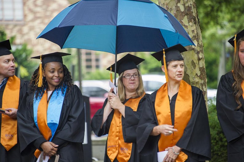 graduates outside the ceremony, one holds an umbrella 