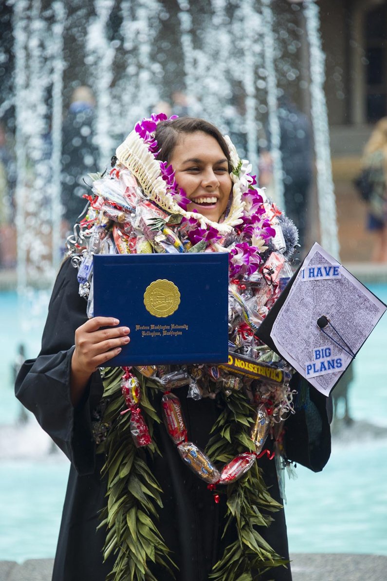 a graduate smiles while wearing so many leis and garlands her ears are covered