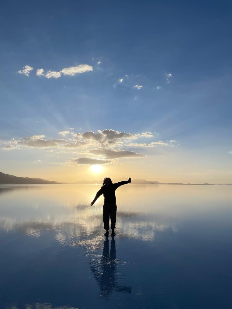 A student poses on a shallow lake; their reflection echoes in the lake's still water.