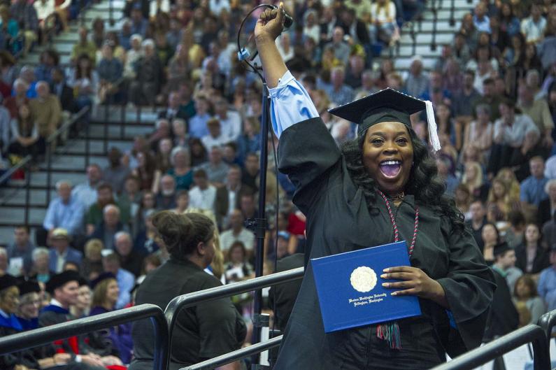 Woman smiling and holding her hand up while holding diploma holder