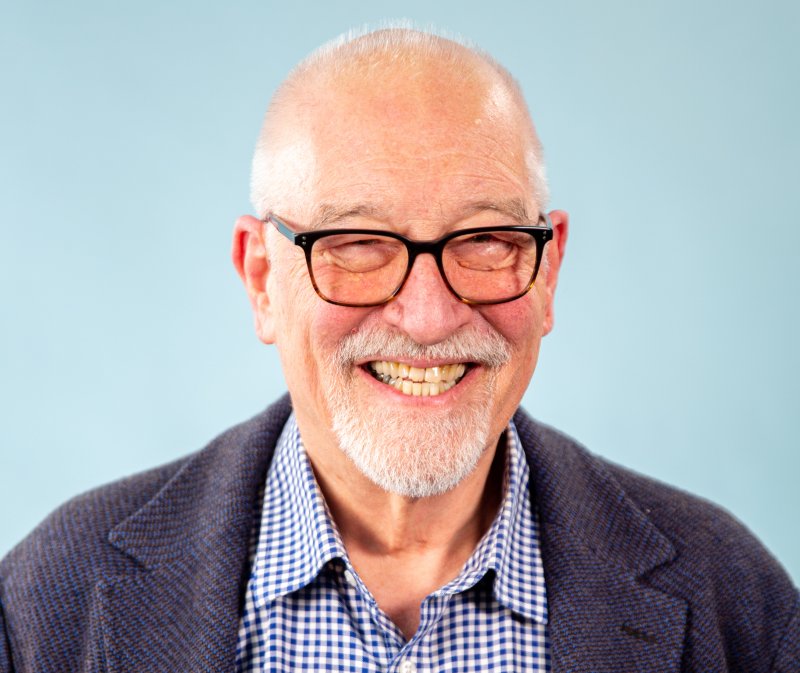 An image of Paul Merriman smiling at the camera in front of a light blue background.
