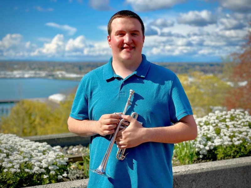 Alex Marbach holds a trumpet while standing on the PAC plaza