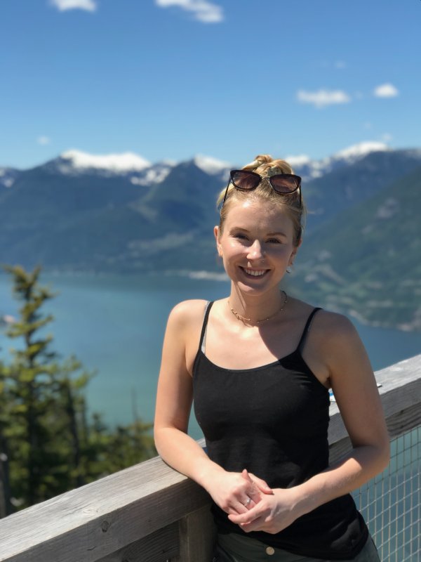 Hannah Hennig stands at a railing with a lake and mountains in the background