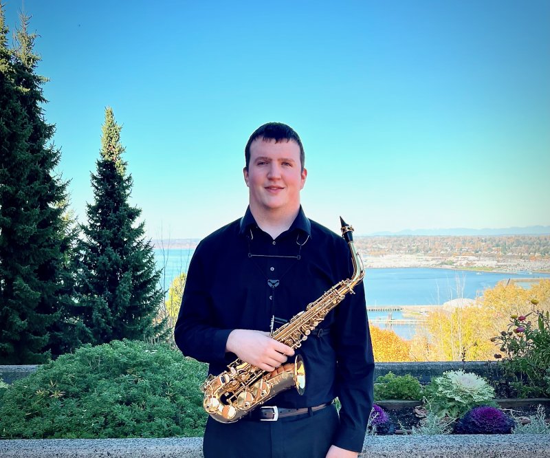 Jordan Marbach stands on the PAC plaza while holding a saxophone 
