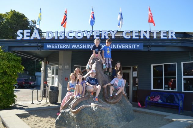 A group of students sit on a sculpture of an octopus in front of WWU's SEA Discovery Center in Poulsbo WA.