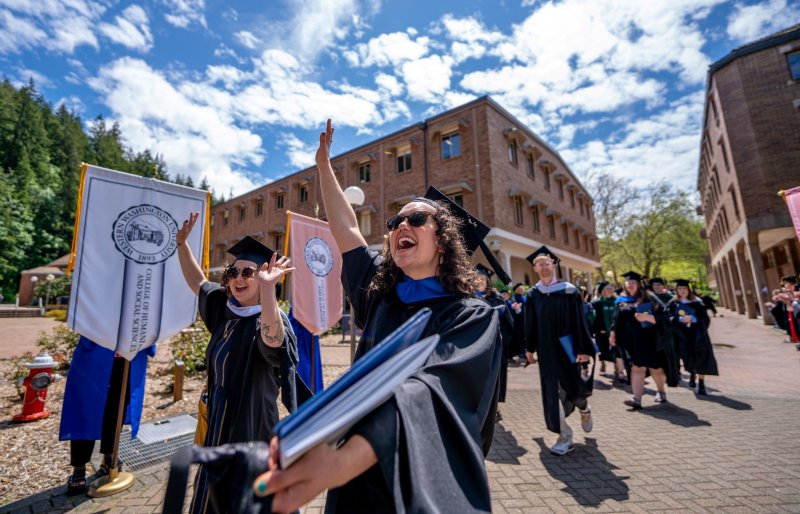 A graduating student smiles with her hand in the air outside.