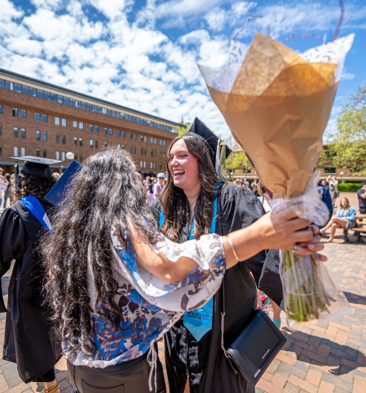 A graduating student hugs a person holding a bouquet.