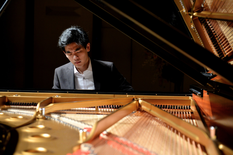 Daniel Hsu plays a piano in a darkened concert hall