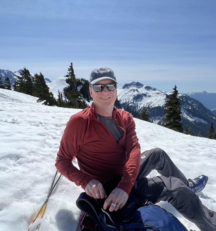 Keith Russell smiles at the camera while sitting in a snowfield high in the Cascades