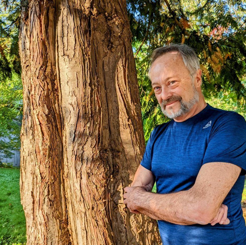 Steve James leans against a tree and smiles at the camera