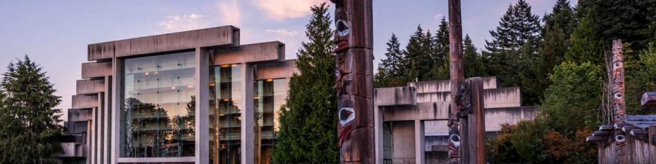 Exterior view of the glass and concrete modernist University of British Columbia Museum of Anthropology, surrounded by totem poles