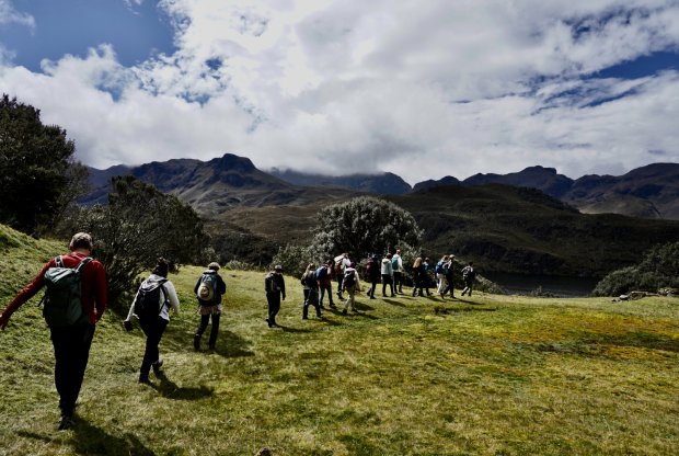 The group walks through El Cajas National Park with mountains ahead under a cloudy blue sky.
