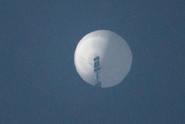 a white balloon carrying some sort of equipment floats in the sky