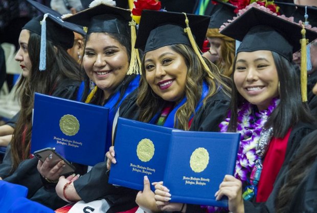 three students show off their diplomas at commencement