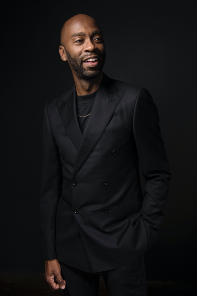 Steve H. Broadnax III stands in a black suit with a black background looking off-camera.