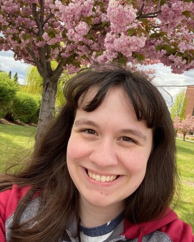 Catherine Baxter smiles for the camera with a tree filled with spring blooms in the background