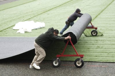 Workers push a dolly loaded with a strip of the new turf for the softball field on south campus in early March. The university renovated the field by replacing the grass with the new turf, among other projects at the field. Photo by Jeremy Smith | Univers