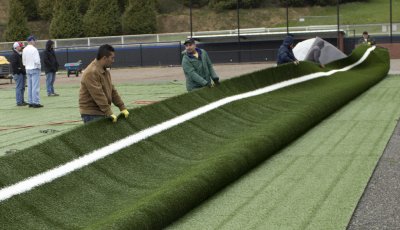Workers flip a roll of turf so they can properly place it along the third base line on the softball field as part of the renovations to the field. Replacing the old grass and fixing the dugouts and fencing were all a part of the renovations during winter 