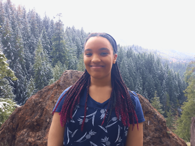 Jaiya Peaks smiles with a forested mountainside behind her