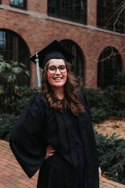 Jillian Mercer smiles while wearing her graduation regalia on campus