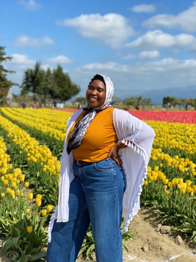 Khadijah Boyker smiles with one hand on her hip, standing before rows of yellow and red tulips