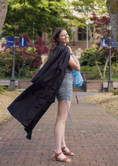 Paige Holman smiles, holding a black commencement robe over her shoulder and looking back at the camera