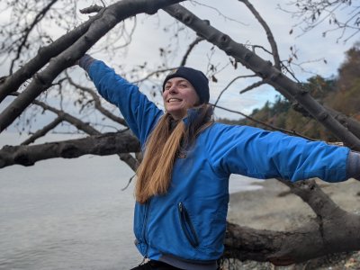 Zoe Hemez smiles and stretches her arms wide to hold the branches of a tree