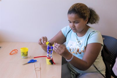 a girl concentrates as she puts together a project with sticks, string, colorful pipe cleaners, and clay
